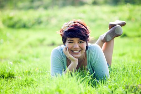 Smiling teenage girl laying in a green grassy field. Shallow depth of field.の写真素材