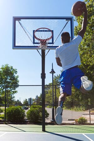 Young basketball player drives to the hoop with a high flying slam dunk. Slight lens flare.