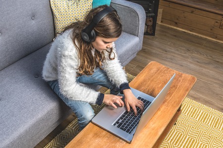 Teenage girl in the Conservatory with nordic sofa, laptop and headphone, wooden floor, yellow rugの写真素材