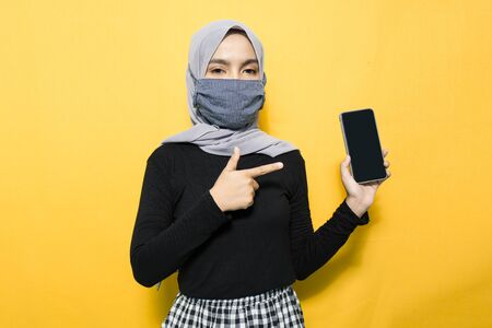 Asian woman wearing mask pointing to hand phoneの写真素材
