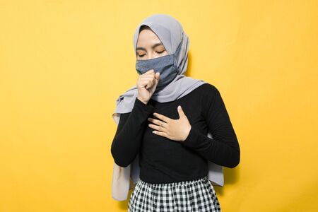 Asian women wearing protective masks, coughing on yellow backgroundの写真素材