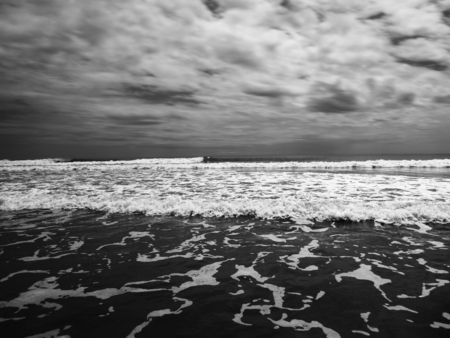 Black and white shot of beautiful white tide wave running on sandy shore in gloomy day. の写真素材