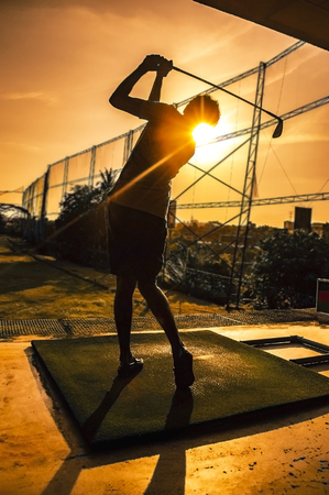 Golfer swinging in orange sunsetの写真素材