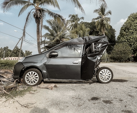 Side view of black smashed small car abandoned on street of remote tropical city of malaysia
