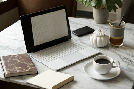 Workstation made of white marble with a book, supplies, and a laptop with a blank screen. Copy space for a product listing or graphic montageの素材