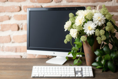 With a keyboard on a wooden table, a white bouquet of fresh flowers, and a blank computer screen against a background of a brick wall, you can see your text, content, or design in the right hand corneの素材