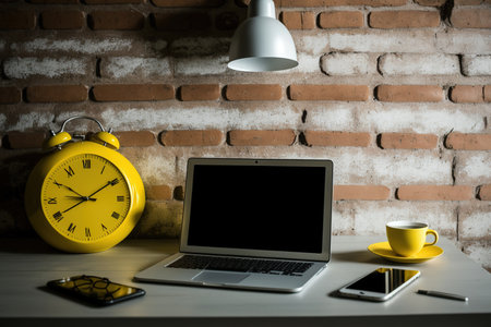 laptop and work supplies are on a table next to a brick wallの素材