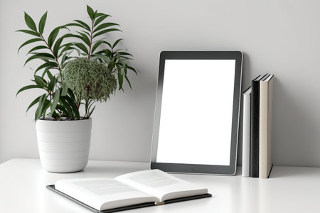 Mock-up computer tablet, plant, and books on white table. Product montage copy spaceの素材