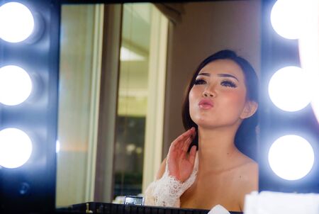 artistic glossy portrait of young beautiful and gorgeous Asian Chinese woman at make up beauty room looking happy admiring reflection on the mirror in style glamour and beauty conceptの写真素材