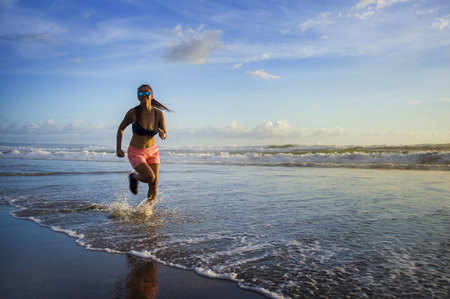 young attractive Asian Chinese sport runner woman in running beach workout on a sunset Summer evening in beautiful sea and coast background in healthy lifestyle and fitness conceptの写真素材