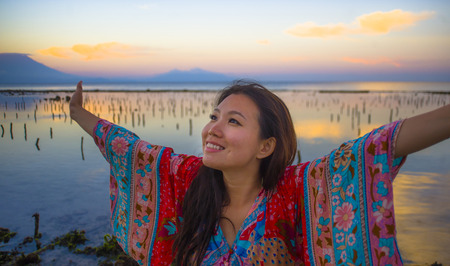 young happy and beautiful Korean woman in traditional Asian dress at sunrise sea landscape looking away with arms opened feeling free enjoying the beach breeze in holidays trip conceptの写真素材