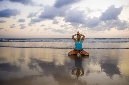 young fit and attractive sport woman in beach sunset yoga practice workout sitting on wet sun in front of the sea in meditation and relaxation exercise in mind and body care and healthy lifestyleの写真素材