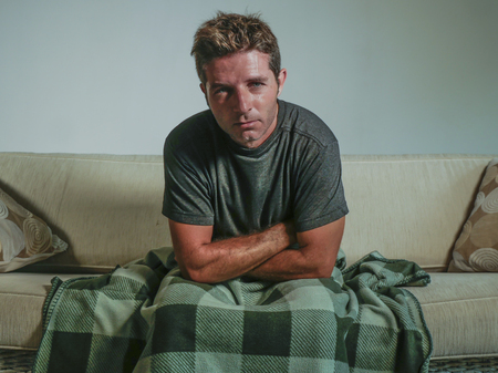 young sad and desperate man at home living room sitting at living sofa couch looking emotional suffering depression and breakdown feeling miserable in depression and lifestyle conceptの写真素材