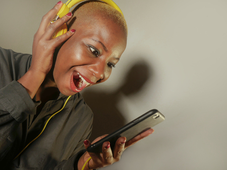 young happy and attractive afro American woman with yellow headphones and mobile phone listening to...