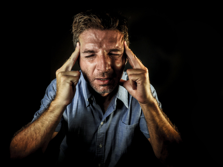 dramatic portrait of attractive sad and depressed man with fingers on his head  desperate suffering depression and headache having problem isolated on black background in sadness and stressの写真素材