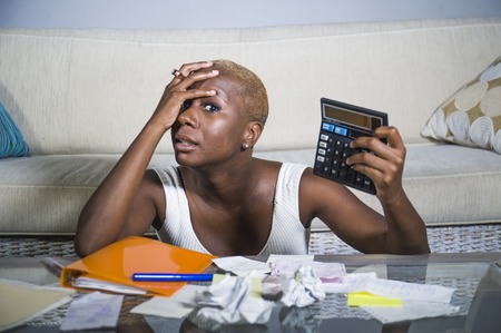 desperate and stressed black afro American woman with calculator and paperwork banking in stress accounting business finance tax and payments in financial mess and problem conceptの写真素材