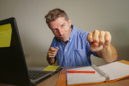 young attractive and happy business man working with laptop computer at home office smiling satisfied and confident pointing finger to camera in successful entrepreneur and winner conceptの写真素材