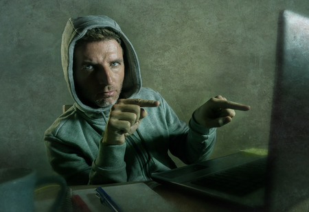 dangerous looking hacker man in hoodie hacking internet computer system pointing his eyes warning...