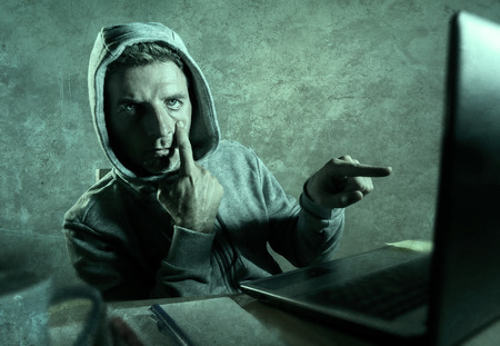 dangerous looking hacker man in hoodie hacking internet computer system pointing his eyes warning about his ability to break password stalking accounts in cyber security conceptの写真素材