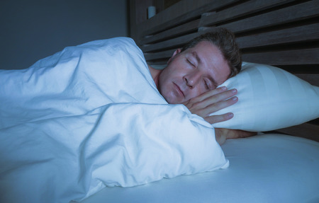 young attractive and handsome tired man on his 30s or 40s in bed sleeping covered with duvet...
