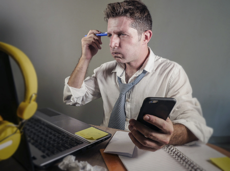 attractive sad and desperate man in lose necktie looking messy and busy working at laptop computer...