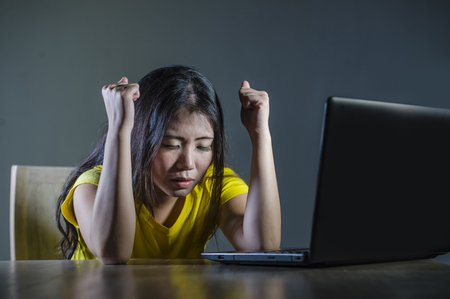 dramatic portrait of scared and stressed Asian Korean teenager girl or young woman with laptop computer suffering cyber bullying stalked and harassed with internet social media password hackedの写真素材
