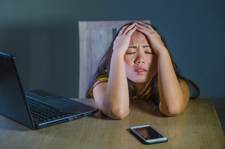 dramatic portrait scared and stressed Asian Korean teen girl or young woman with laptop computer and mobile phone suffering cyber bullying stalked and harassed with internet password hackedの写真素材