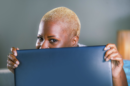 close up lifestyle portrait of young classy attractive and happy black african american woman posing playful hiding behind laptop computer screen smiling cheerful and relaxed の写真素材