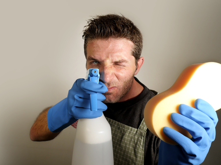 young attractive and happy domestic house husband or single man holding sponge and detergent spray as a gun pointing to the camera in washing gloves in home cleaning service workの写真素材