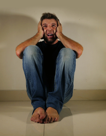 young desperate and depressed man crying alone sitting at home floor in shady and dramatic studio...