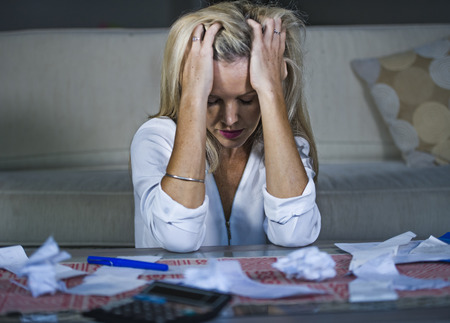 attractive worried and desperate blond woman calculating domestic money expenses doing paperwork and...