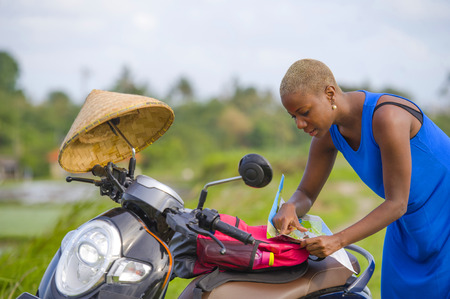 young beautiful black afro american tourist woman with scooter motorbike looking to road map searching the way exploring fields in Asia holidays summer travel and digital nomad lifestyleの写真素材