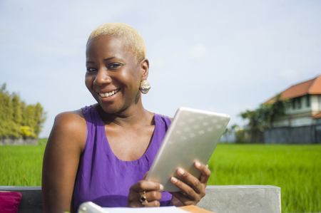 young attractive and happy successful black afro american woman working with digital tablet pad outdoors on green field cafe smiling cheerful in digital nomad success and online freelance jobの写真素材