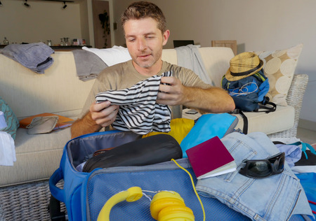 young attractive and happy man at home couch preparing travel back and packing suitcase folding clothes and organizing passport and things before leaving on holidays trip and travel conceptの写真素材