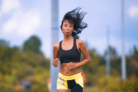fit and sporty Asian Thai woman with athletic body training outdoors in hard running workout on green field landscape doing jogging workout in sport fitness and healthy lifestyle conceptの写真素材