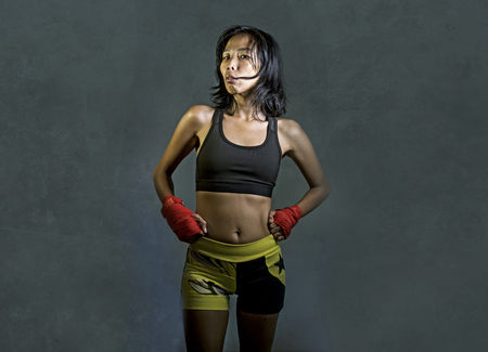 portrait of sporty and fit fighter Asian Chinese woman using wrist wraps training mma fight sport or boxing workout looking dangerous in badass pose isolated on dark grunge backgroundの写真素材