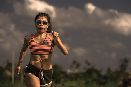 athletic and fit runner Asian woman training running series workout working hard outdoors on field background in harsh contrast light sport advertising style on energy and sacrifice conceptの写真素材