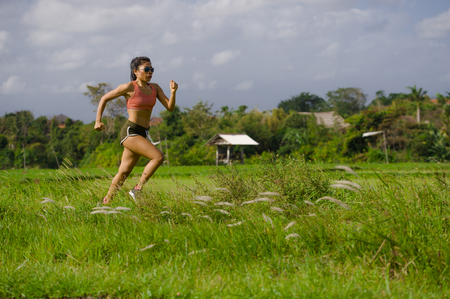 attractive and very fit Asian sport woman training running workout at green field landscape background working hard in healthy lifestyle and competitive female runner jogging conceptの写真素材