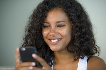 lifestyle isolated portrait of young happy and beautiful hispanic woman at home using mobile phone networking and texting relaxed on couch smiling cheerful enjoying internet social mediaの写真素材