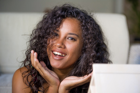 lifestyle portrait of young gorgeous and happy exotic black hispanic woman looking at the camera seductive after applying make up at home in beauty fashion and skin conceptの写真素材