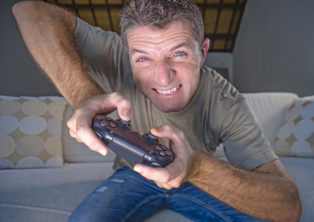 lifestyle portrait of young stressed and excited gamer man playing video game at home living room...