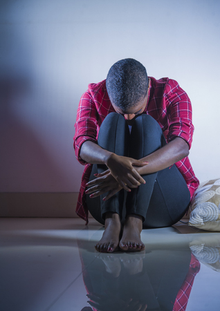lifestyle indoors shady portrait of young sad and depressed black afro American woman sitting at home floor feeling desperate and worried suffering pain and depression in dramatic lightの写真素材