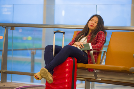 lifestyle portrait of young pretty tired and exhausted Asian Korean tourist woman in airport sleeping bored sitting at boarding gate hall waiting for delayed or canceled flightの写真素材