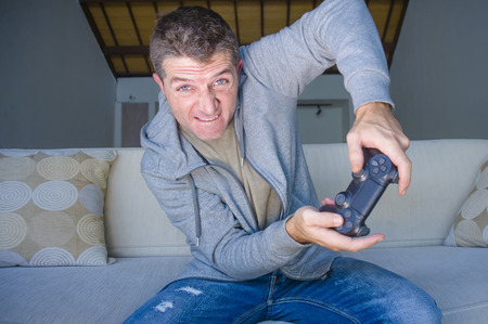 lifestyle portrait of young stressed and excited gamer man playing video game at home living room...