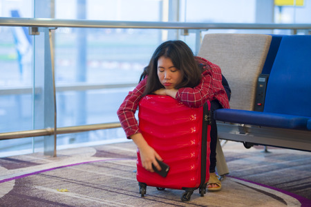 lifestyle portrait of young pretty tired and exhausted Asian Korean tourist woman in airport sleeping bored sitting at boarding gate hall waiting for delayed or canceled flightの写真素材