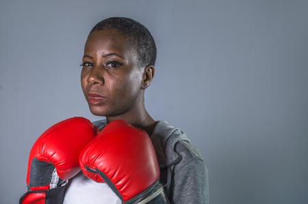 close up face portrait of young angry and defiant black afro American sport woman in boxing gloves training and posing as a dangerous fighter in fitness gym and fight workout conceptの写真素材