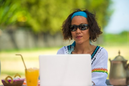 lifestyle outdoors portrait of young happy and attractive afro american mixed ethnicity woman working with laptop computer from beautiful cafe in successful freelance internet job conceptの写真素材