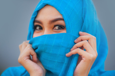 lifestyle isolated background portrait of young beautiful and happy Asian woman in hijab muslim head scarf covering her face playful having fun and smiling cheerfulの写真素材