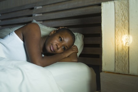 lifestyle night portrait of young sad and stressed black african American woman lying on bed upset...