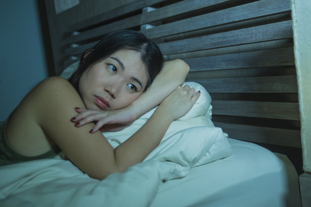 lifestyle night portrait of young beautiful depressed and sad Asian Chinese woman having insomnia lying in bed sleepless suffering anxiety stress and depression problem thinking worriedの写真素材